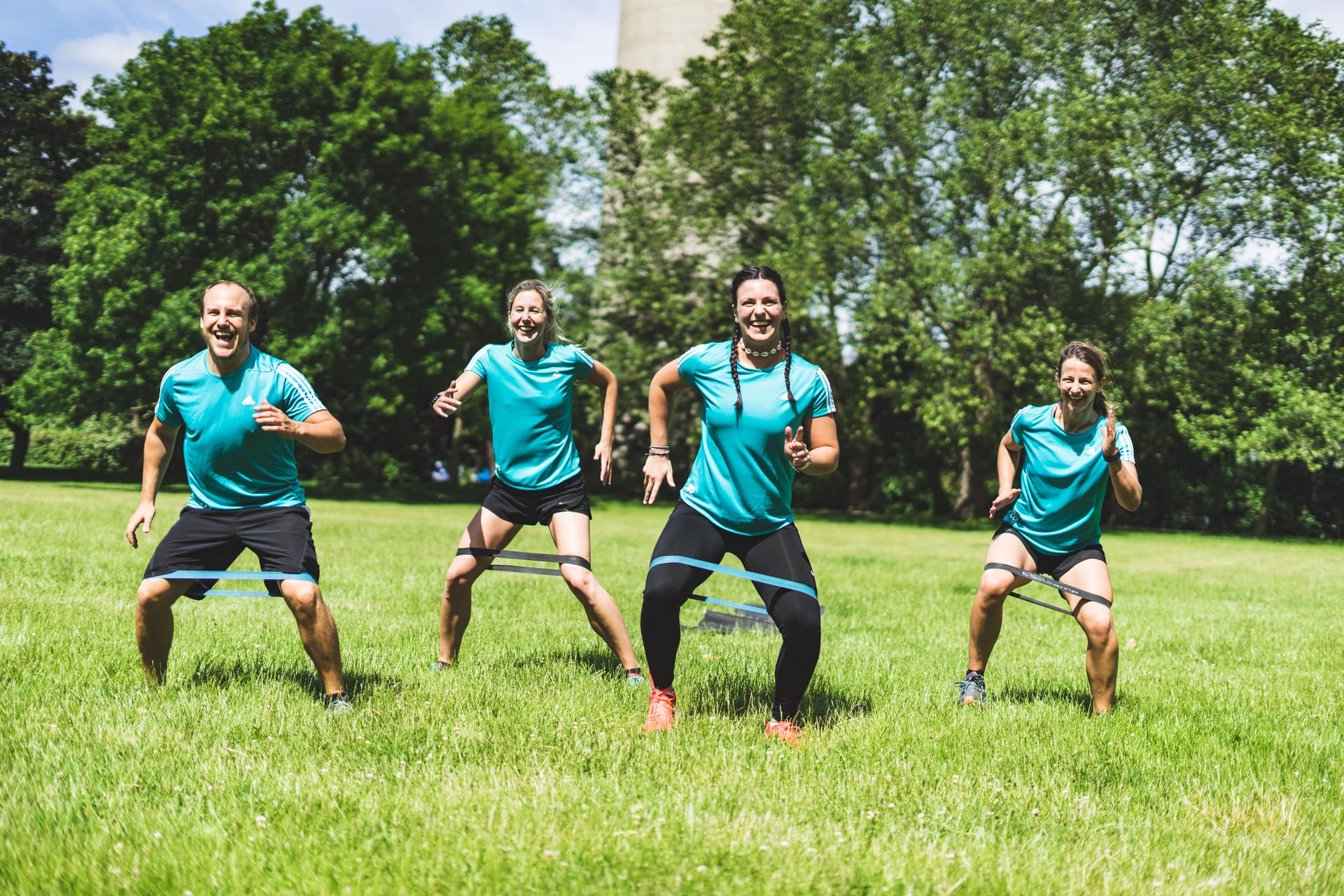 Vier Outdoor Trainer/innen trainieren auf einer grünen Wiese