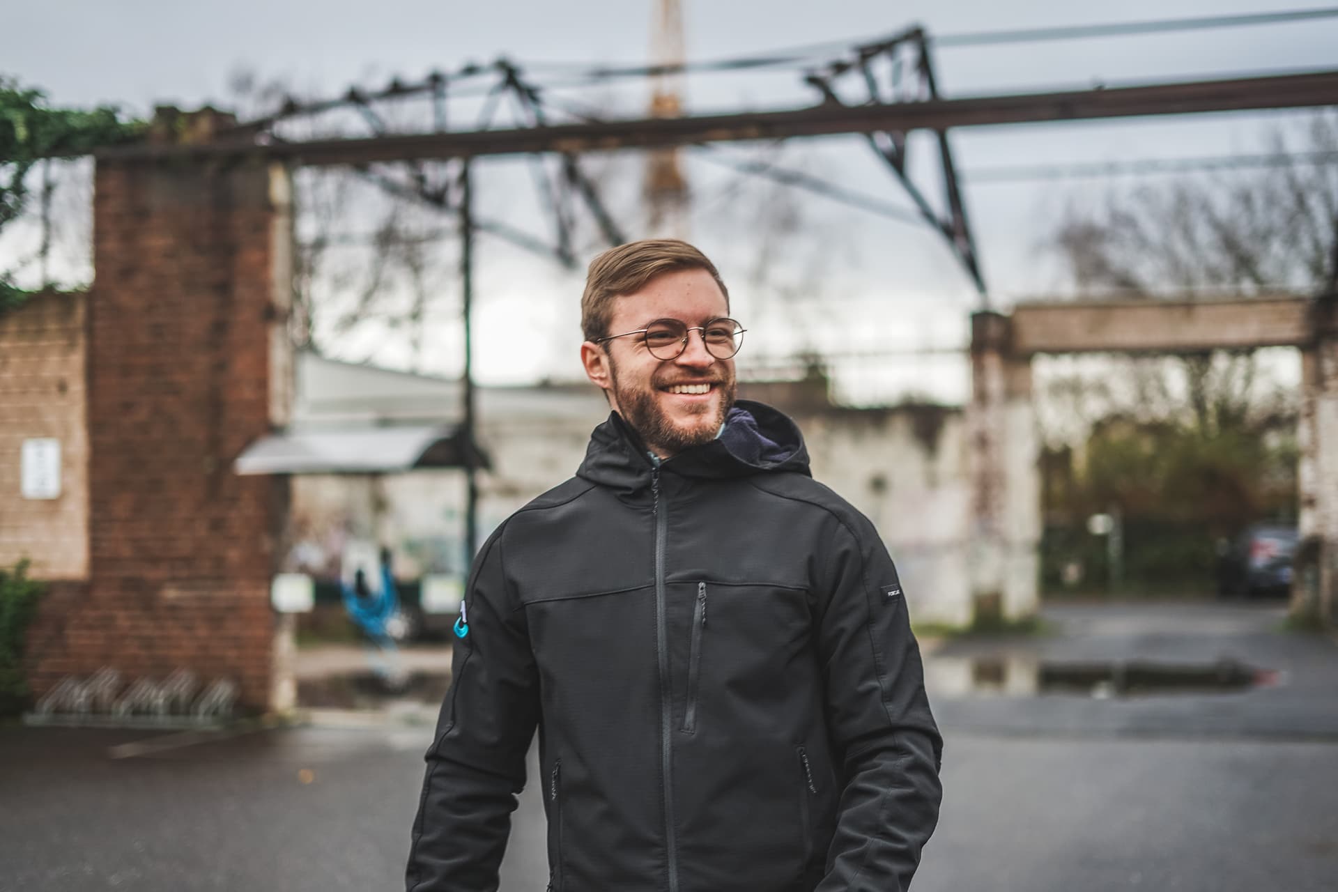 Motivierter Fitness Coach in schwarzer Outdoor-Jacke auf einem urbanen Trainingsgelände, bereit für Outdoor-Training