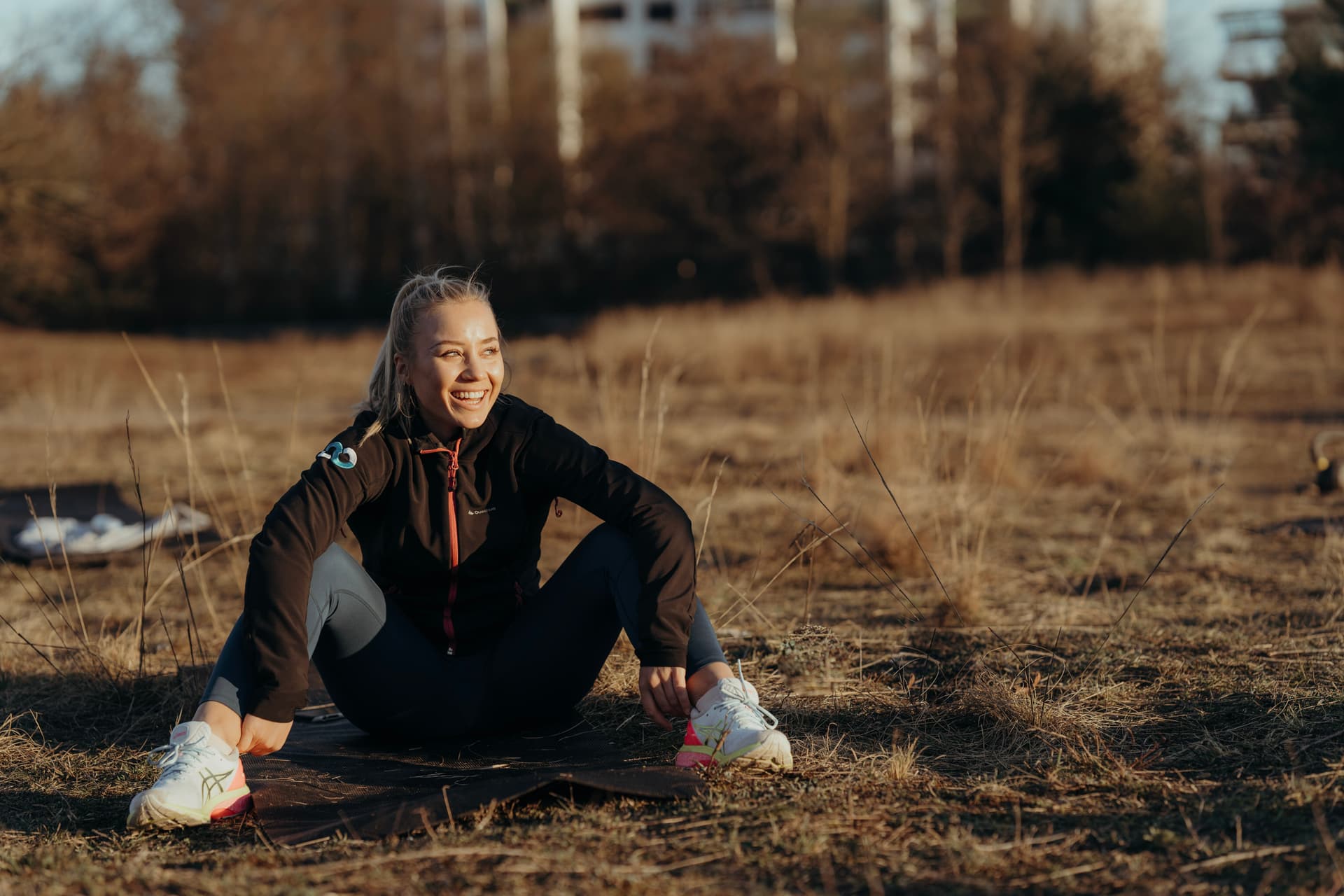 Frau macht eine Workoutpause und sitzt im freien auf einer Matte mit füßen aufgestellt