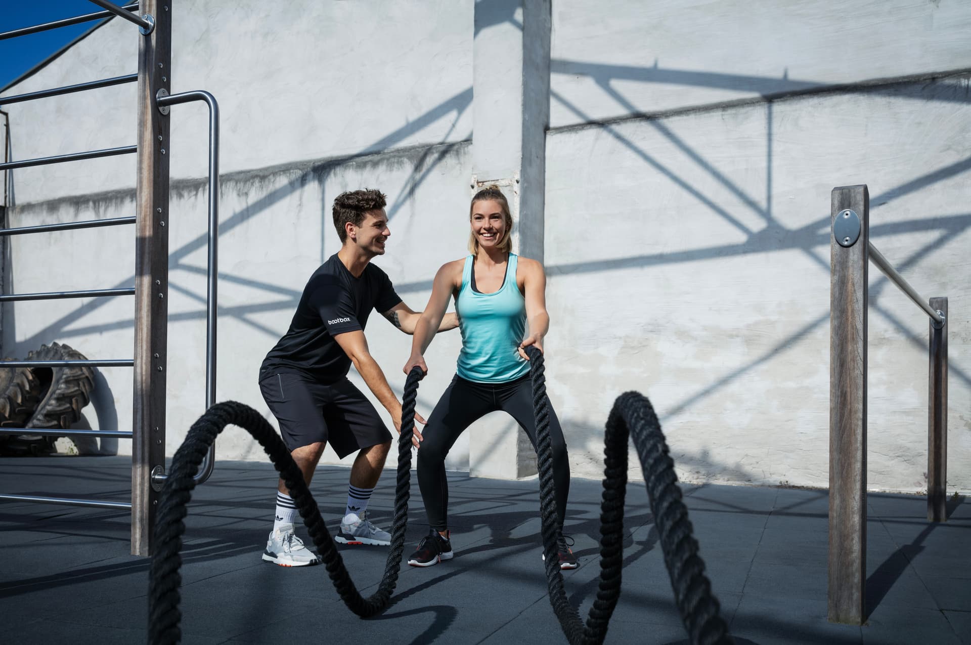 Die Athletin ist an am Battle rope und der Trainer steht neben ihr und korrigiert ihre Haltung.