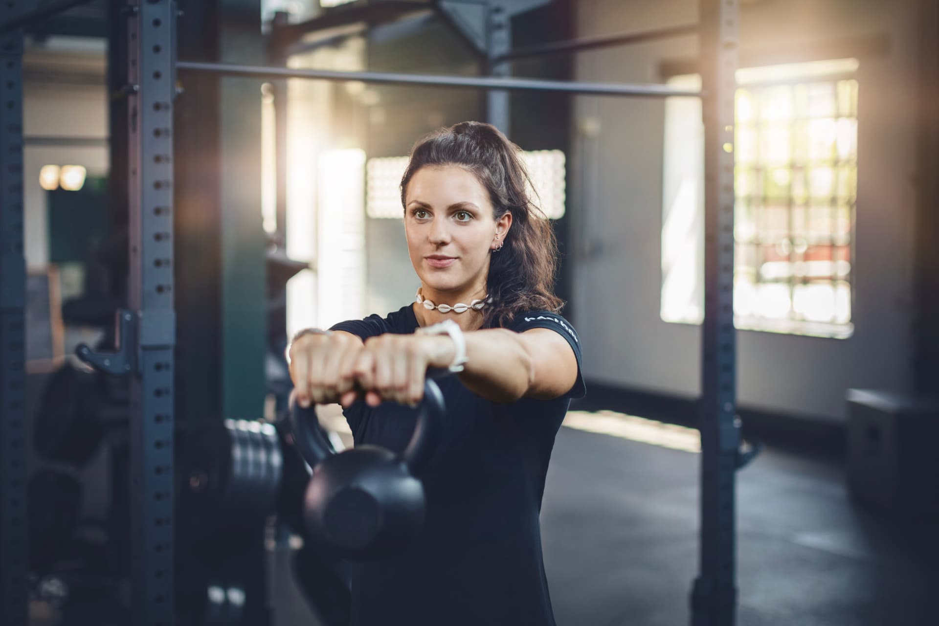 Eine Frau hält eine Kettlebell mit gestreckten Armen nach vorne