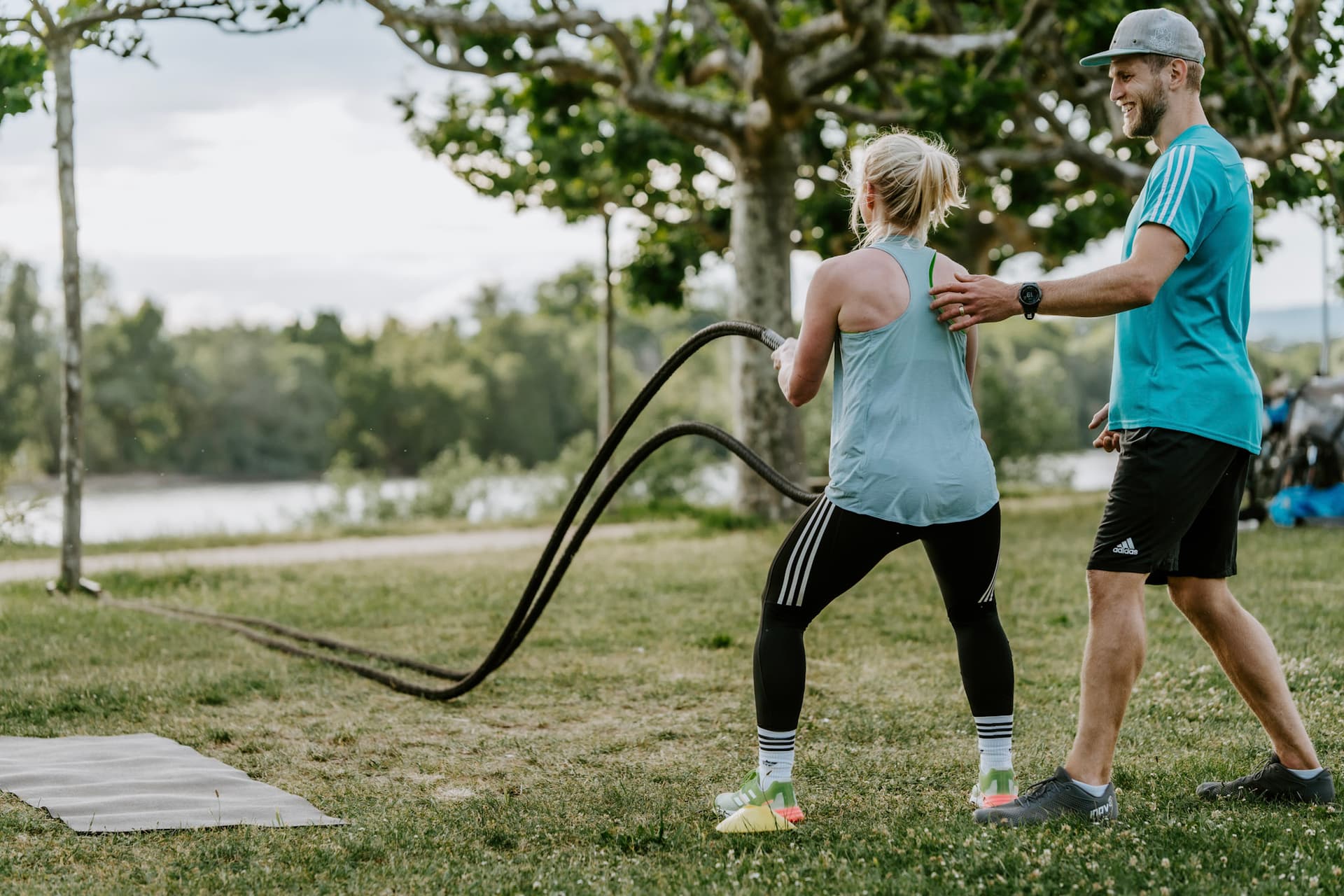 Teilnehmerin ist am Battle Rope. Der Trainer steht neben ihr mit der hand am Rücken und korrigiert ihre Haltung.