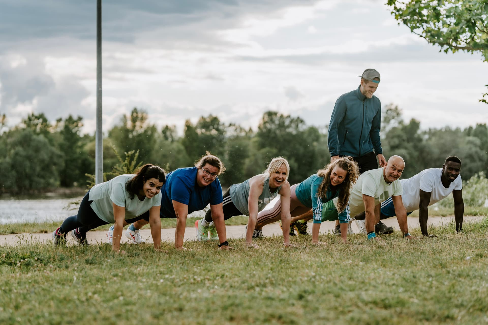 Bootcamp Kurs Teilnehmer sind alle in der Plank Position in einer Reihe. Trainer steht hinter ihnen.