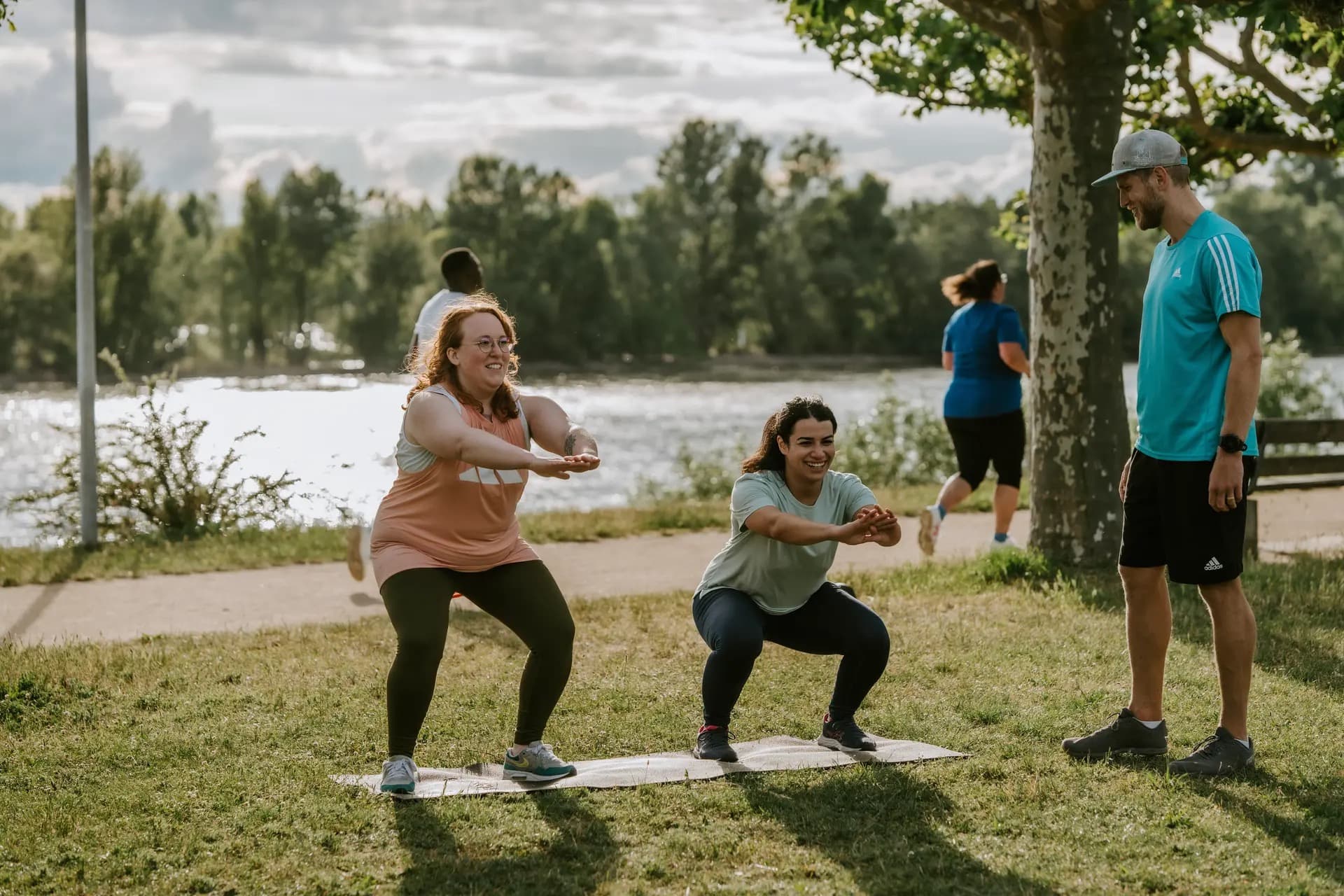 Zwei Frauen machen Kniebeugen während eines Outdoor Bootcamps in Köln, Friedenspark angeleitet von einem Personal Trainer. Fitness in der Natur für alle Levels.