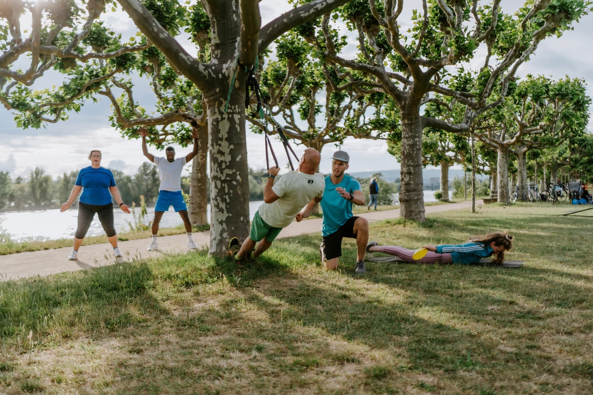 Mann trainiert mit TRX-Bändern an einem Baum in Köln, Friedenspark, angeleitet von einem Outdoor Personal Trainer. Funktionelles Training für Kraft und Stabilität.