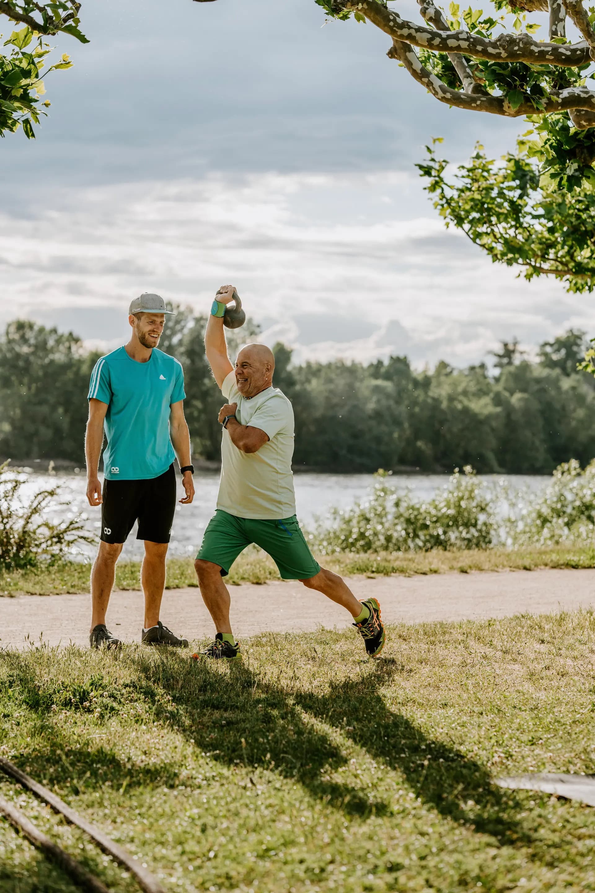Personal Trainer unterstützt einen Teilnehmer bei einer Kettlebell-Übung in Köln, Beethovenpark. Funktionelles Training im Freien mit motivierender Atmosphäre.