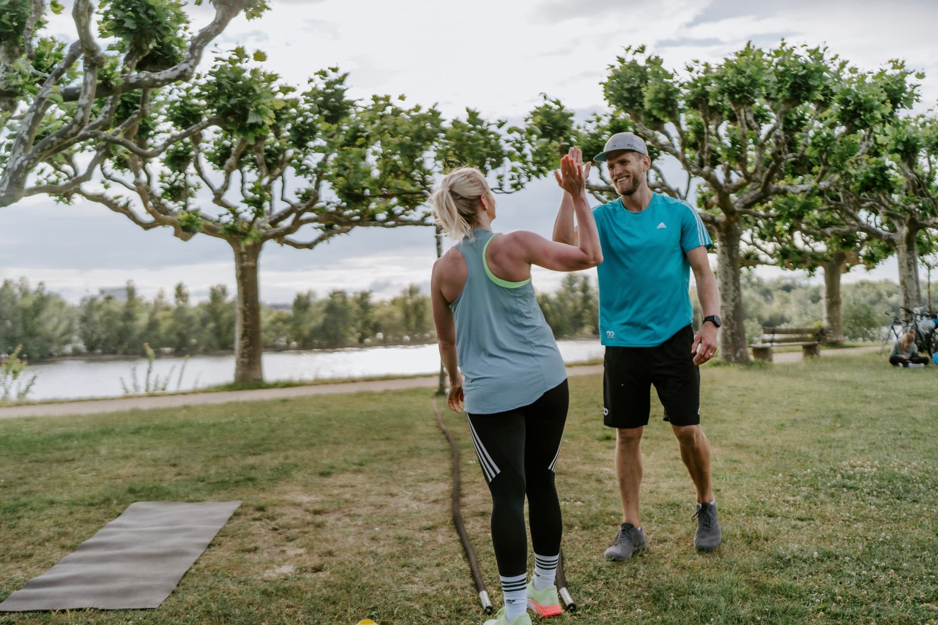 Teilnehmerin eines Outdoor Bootcamps in Göttingen, Schillerwiesen gibt ihrem Trainer ein High-Five nach dem Training. Teamspirit und Motivation beim Sport in der Natur.