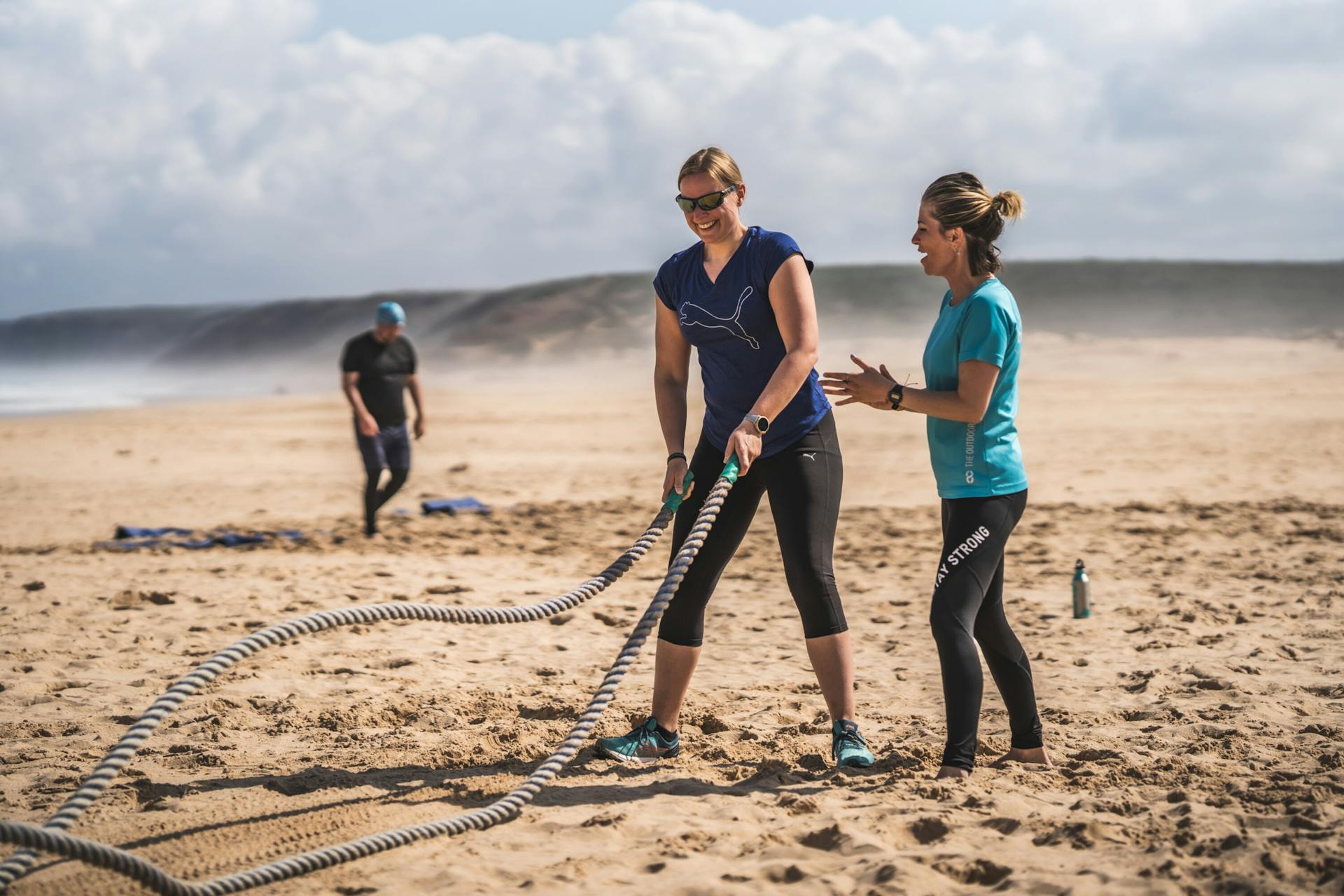 Personal Trainer betreut Reiseteilnehmerin am Strand mit Ropes