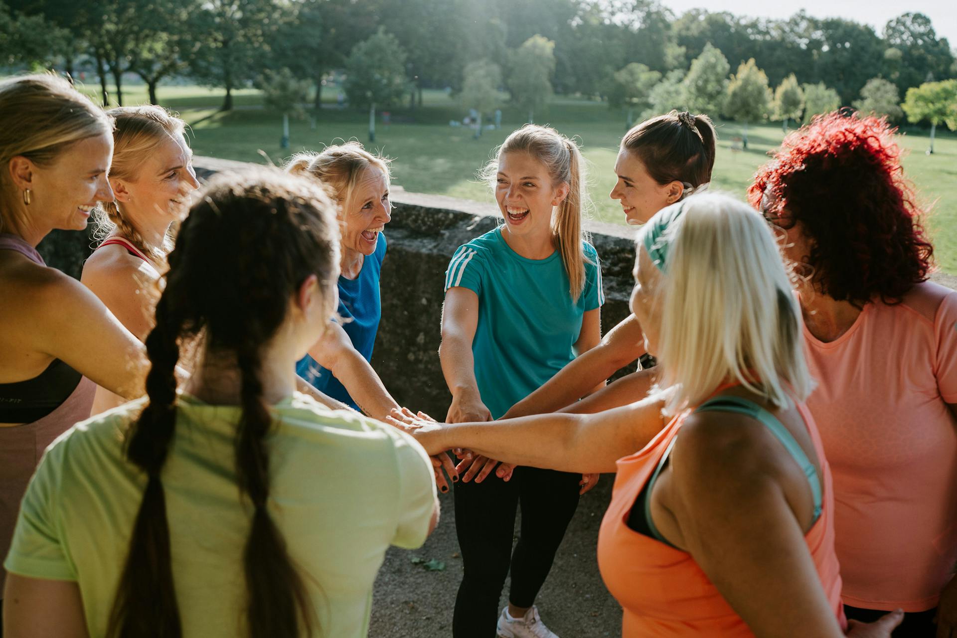 Eine Frauen Trainingsgruppe steht im Kreis mit den Händen ausgestreckt in die Mitte und feiern sich für ihr tolles Training