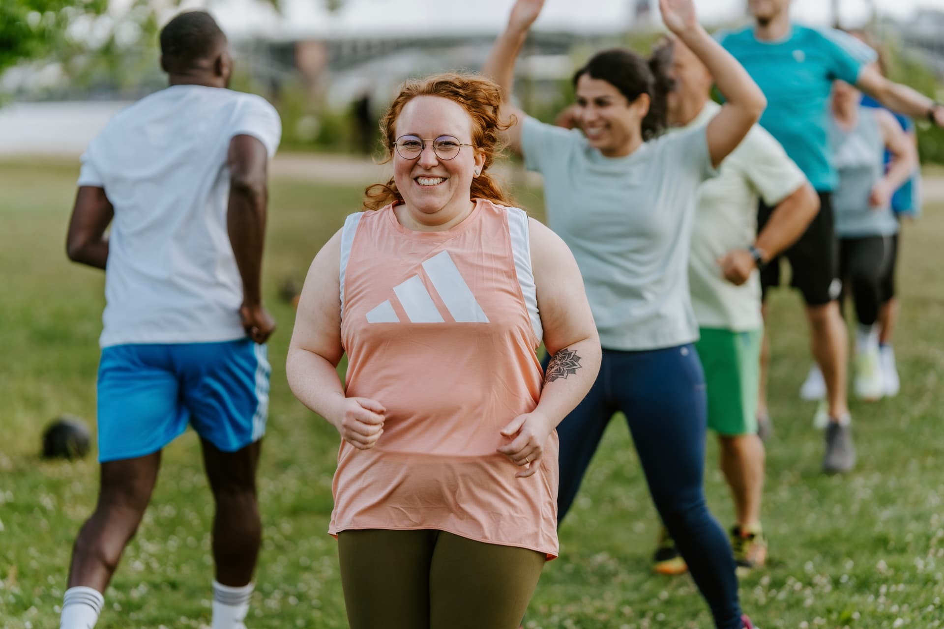 Eine Sportlerin im rosa Top hüpft gut gelaunt im Outdoor Training bei Original Bootcamp