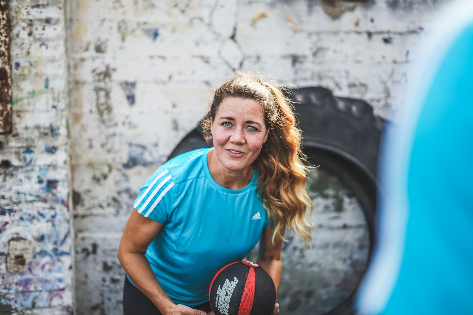 Personal Trainerin Natalie blickt in die Kamera und hält einen Medizinball