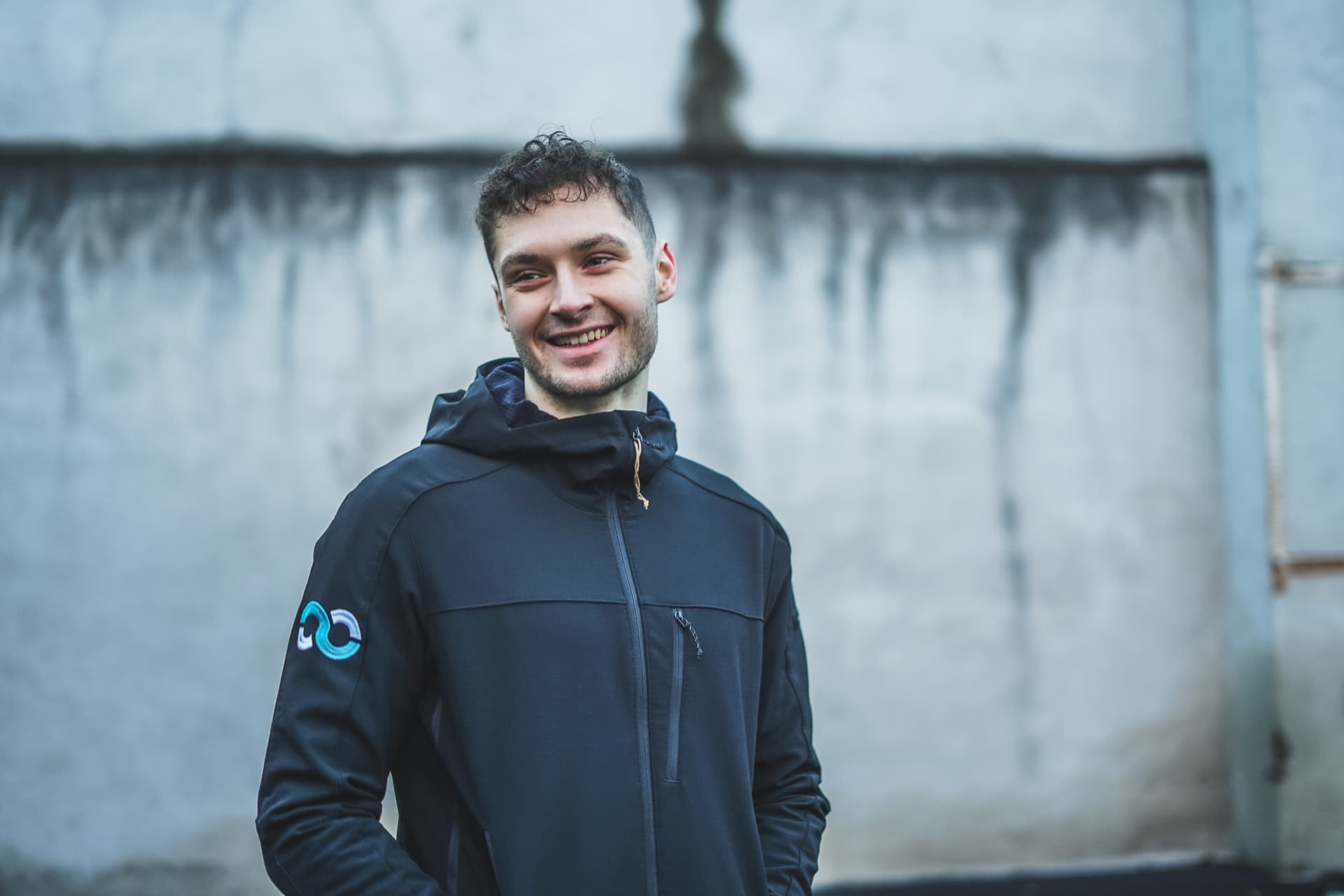 Max Höflich aus Mainz steht vor einer grauen Wand und führt lachend einen Deadlift aus