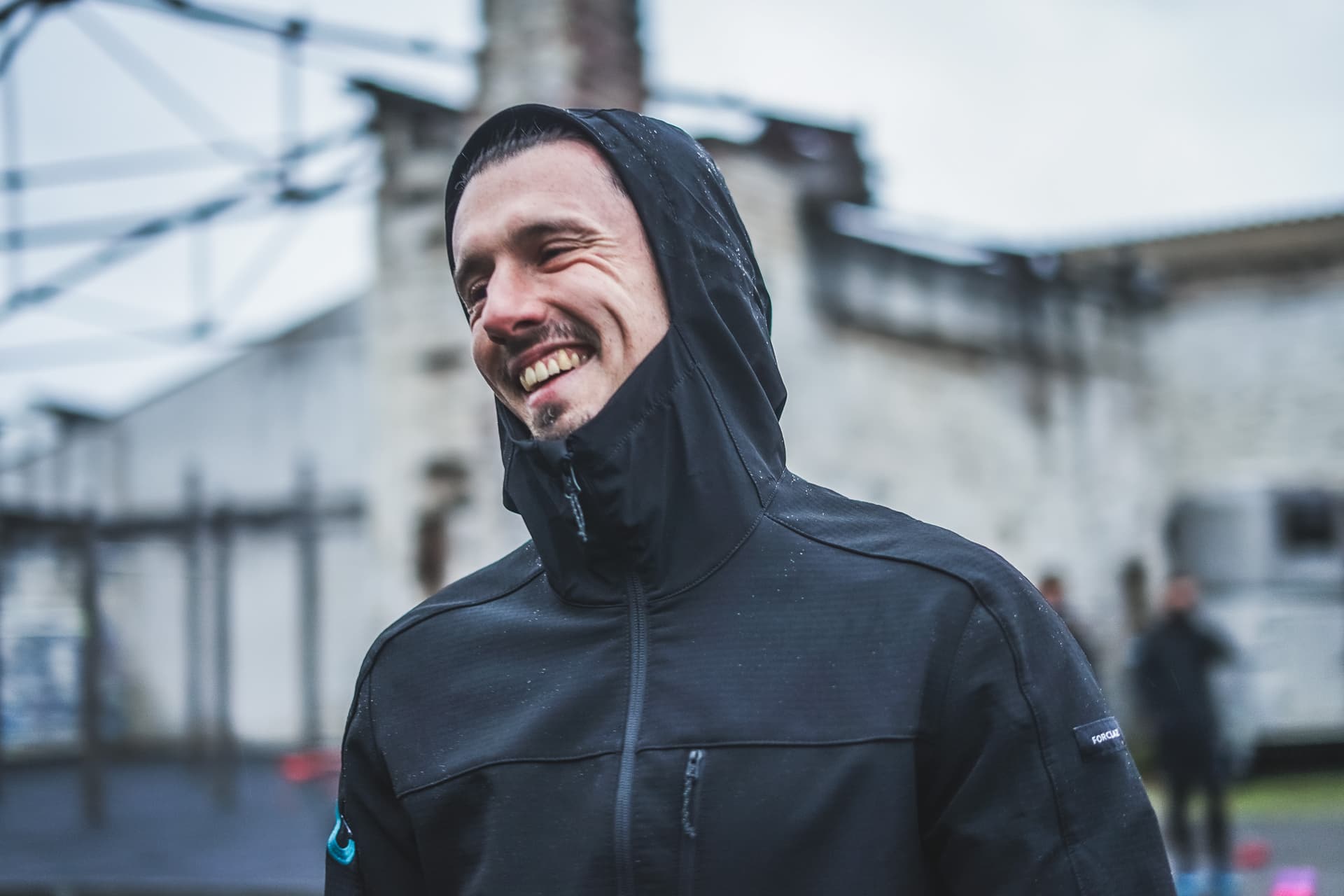 Personal Trainer Robert Biller aus Frankfurt, lächelnd in einer schwarzen Jacke mit Kapuze, Outdoor-Umgebung