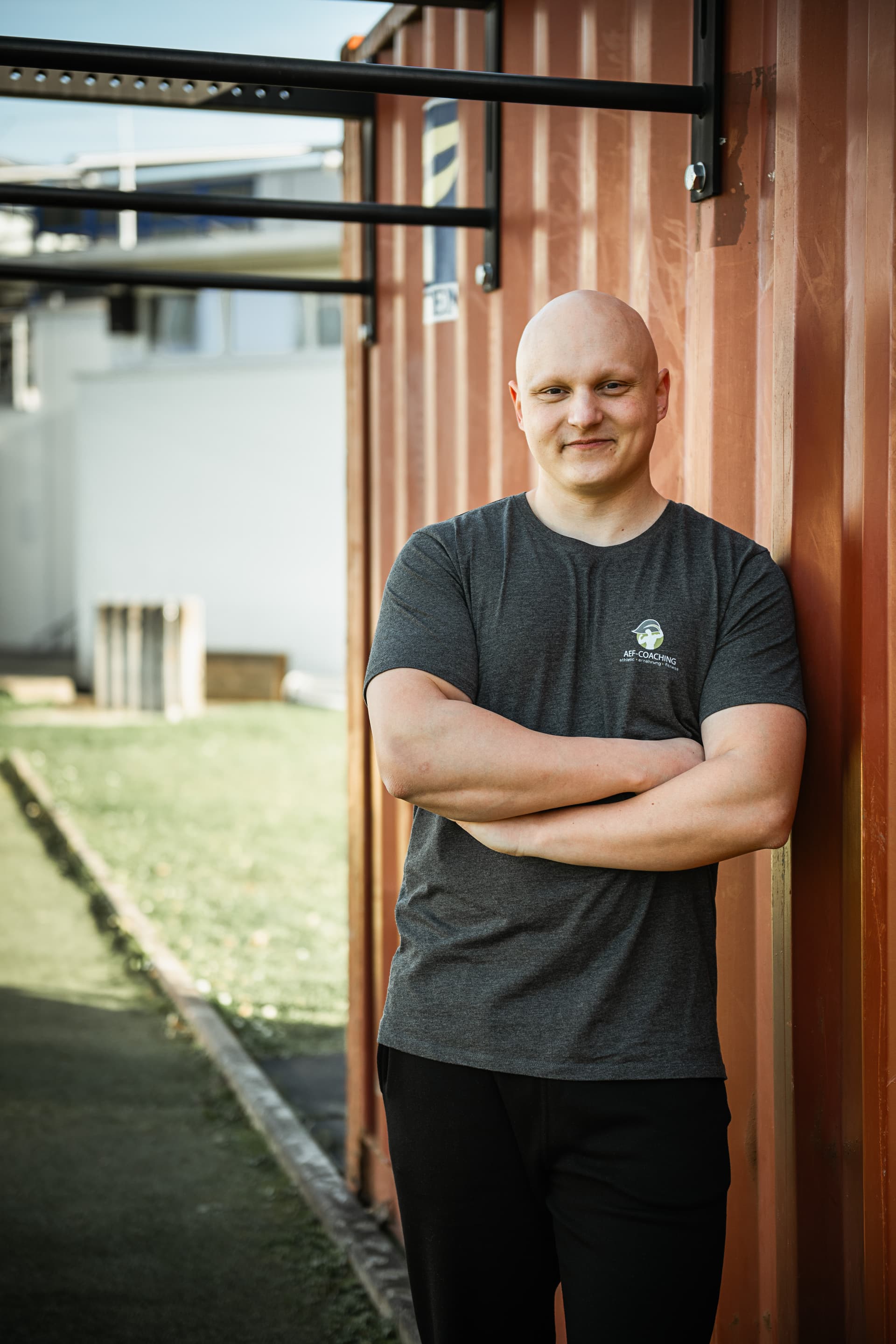 Fitness Trainer Tobias Schmitt lächelt und lehnt an eine Wand