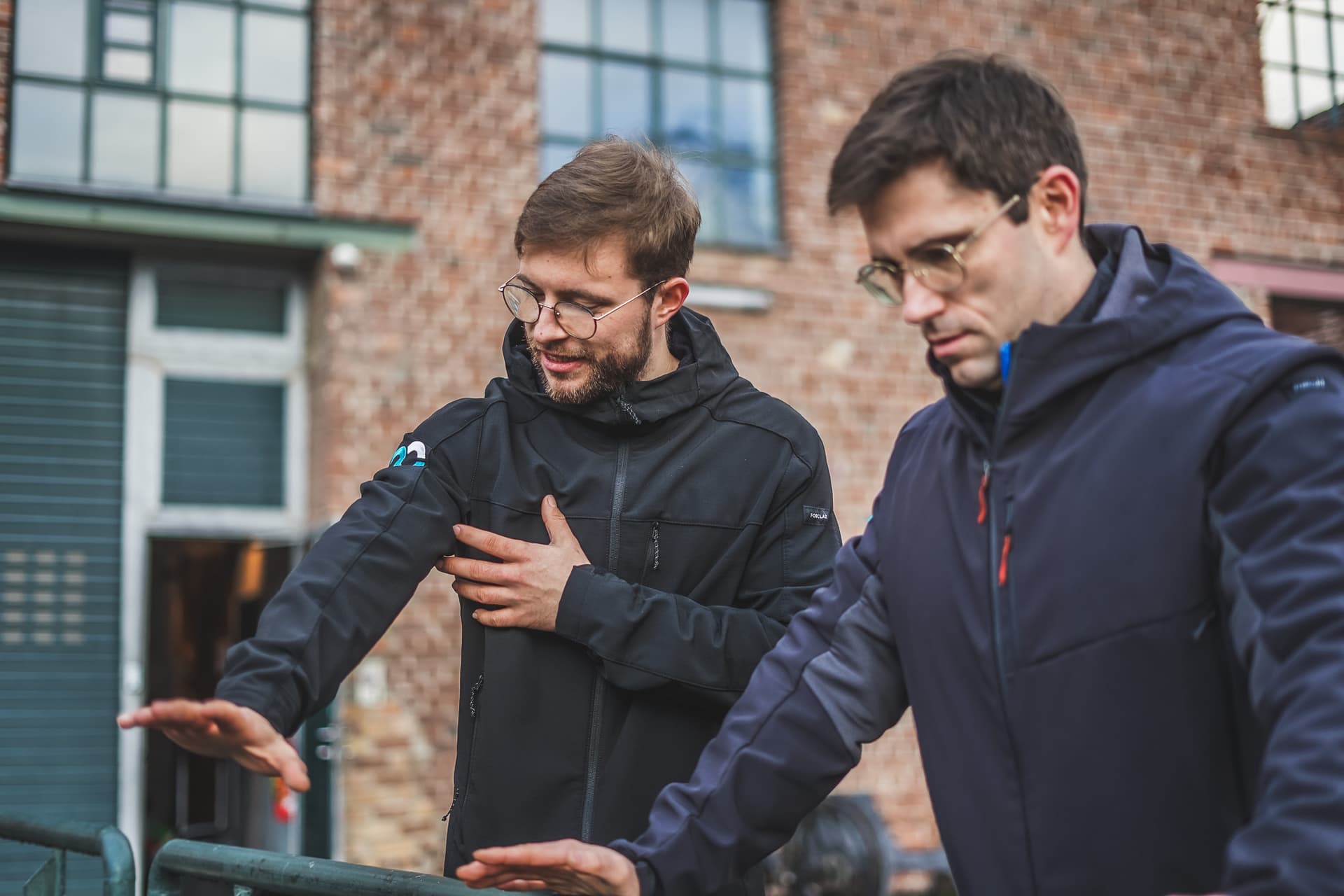 Personal Trainer gibt einem Kunden Anweisungen in einem Outdoor-Trainingssetting, beide in funktionaler Outdoor-Kleidung.