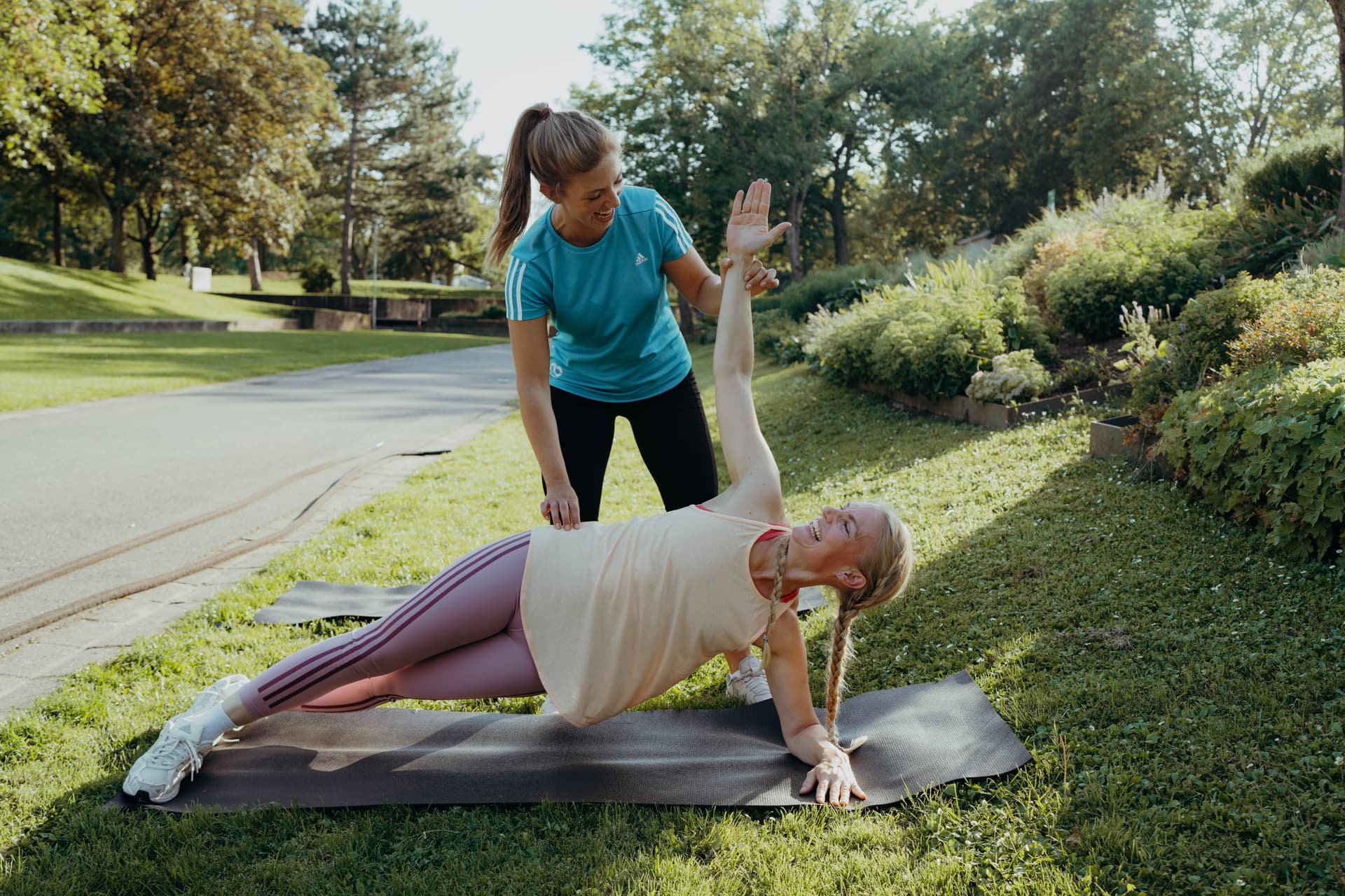 Eine Teilnehmerin trainiert fröhlich gemeinsam mit ihrer Trainerin auf einer Matte beim Outdoor Bootcamp in Hannover.