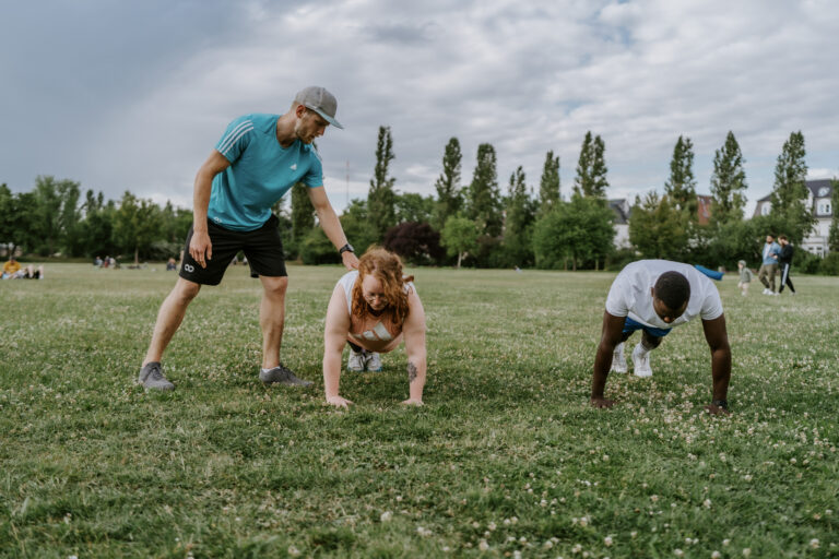Trainer leitet Bootcamp-Gruppe an: Mehrere Personen machen Liegestütze im Park beim Outdoor-Zirkeltraining