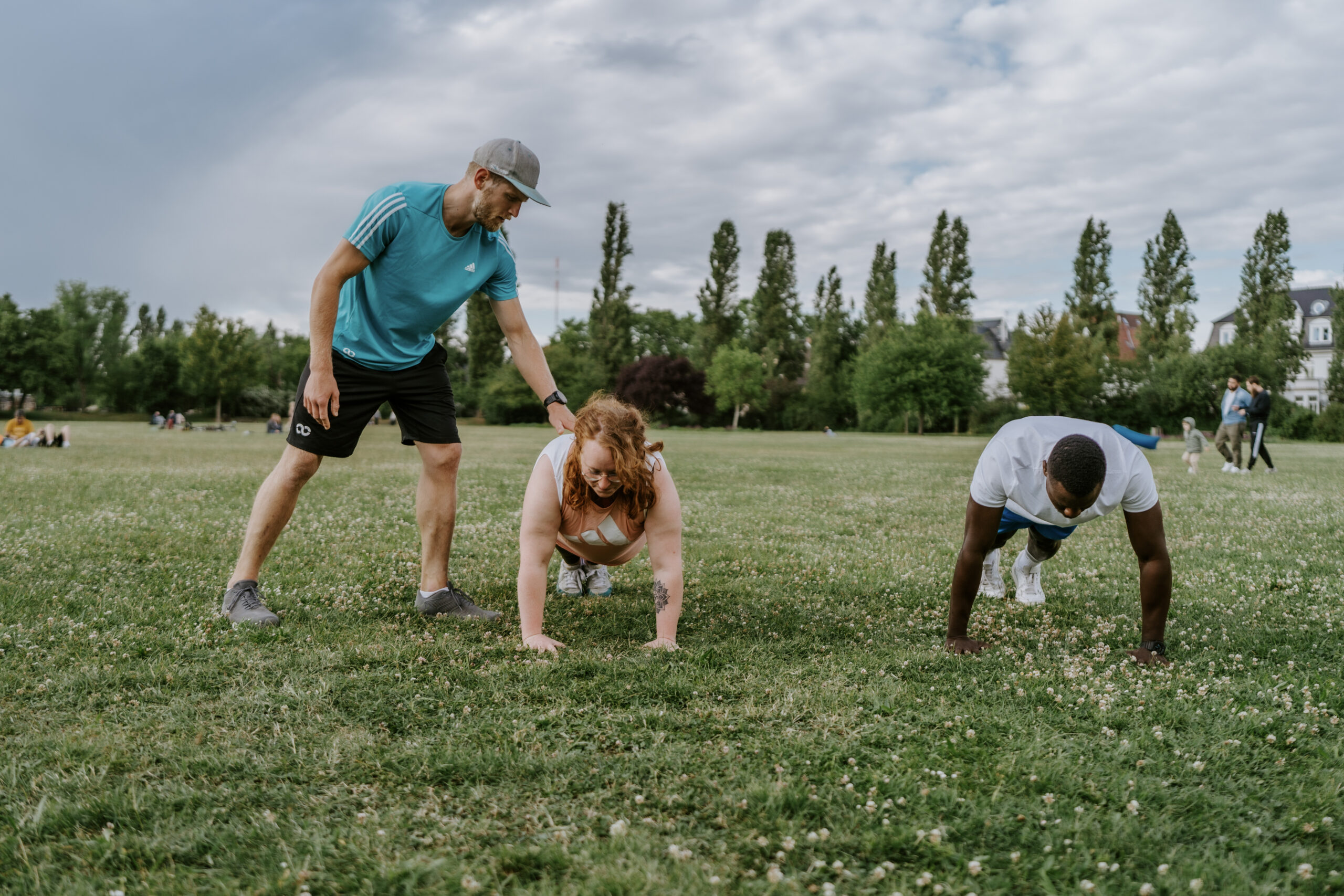 Trainer leitet Bootcamp-Gruppe an: Mehrere Personen machen Liegestütze im Park beim Outdoor-Zirkeltraining