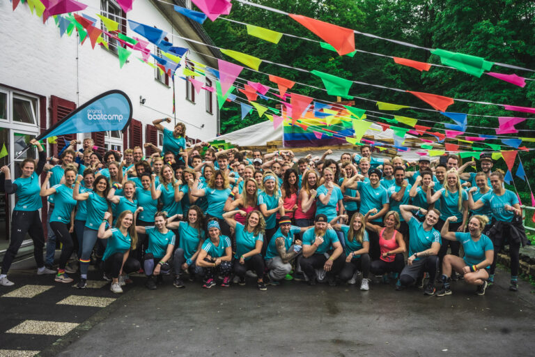 Große Trainingsgruppe Original Bootcamp in türkisen Shirts bei Outdoor-Event, Team-Foto mit bunten Wimpeln