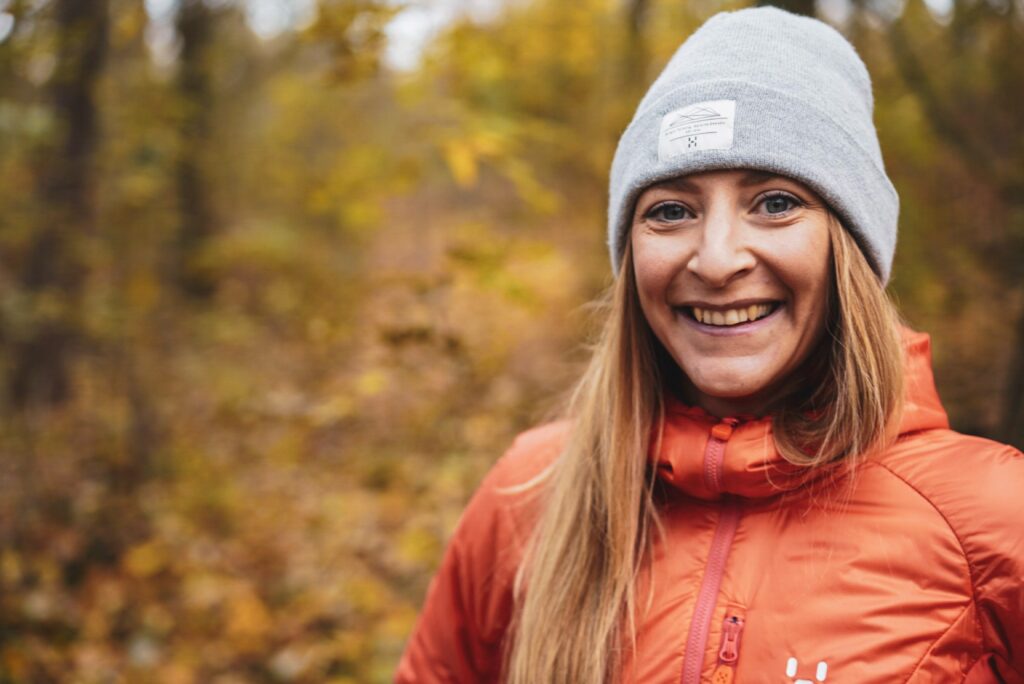 Geschenk für Sportler: Funktionsmütze und Funktionsjacke Geschenk für Sportler: Lachende Frau mit grauer Funktionsmütze und Funktionsjacke im Herbstwald