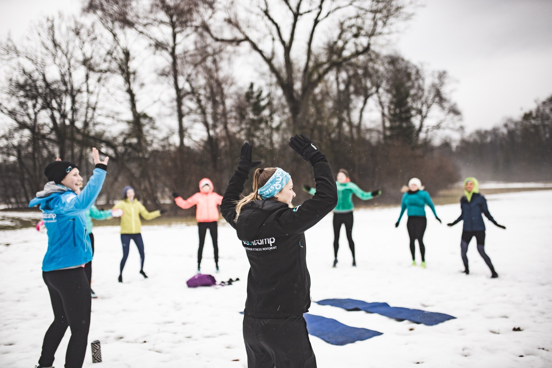 Fitness Geschenk für Frauen: Eine Gruppe wärmt sich beim Outdoor-Training im Schnee mit erhobenen Armen auf
