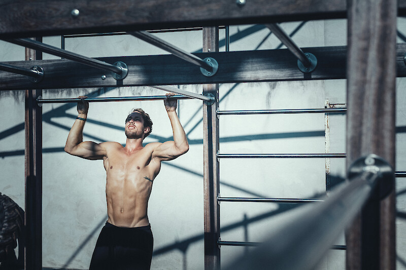 Athlet beim Klimmzug-Training an einer Outdoor-Station – funktionelles Zirkeltraining für Muskelaufbau und Oberkörperkraft.