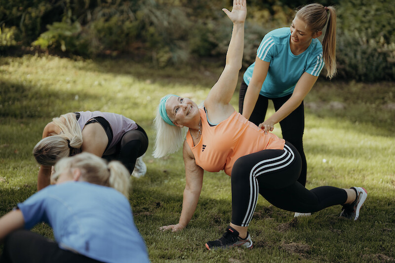 Trainerin unterstützt Teilnehmerin beim Aufwärmen im Outdoor Zirkeltraining – Beweglichkeit und Technik als Grundlage für effektiven Muskelaufbau.