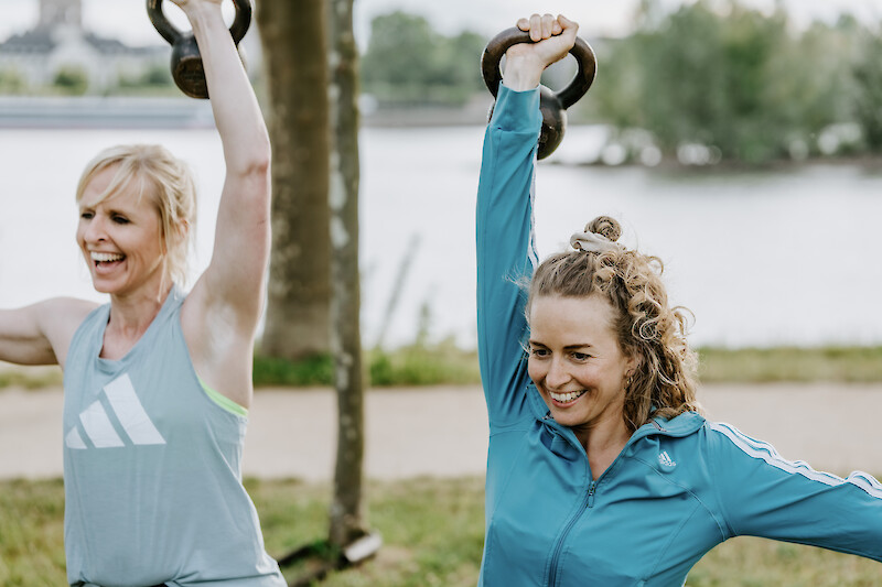 Zwei Frauen führen Kettlebell-Übungen beim Outdoor Zirkeltraining aus – effektives Training zur Stärkung der Muskulatur und zum Muskelaufbau.
