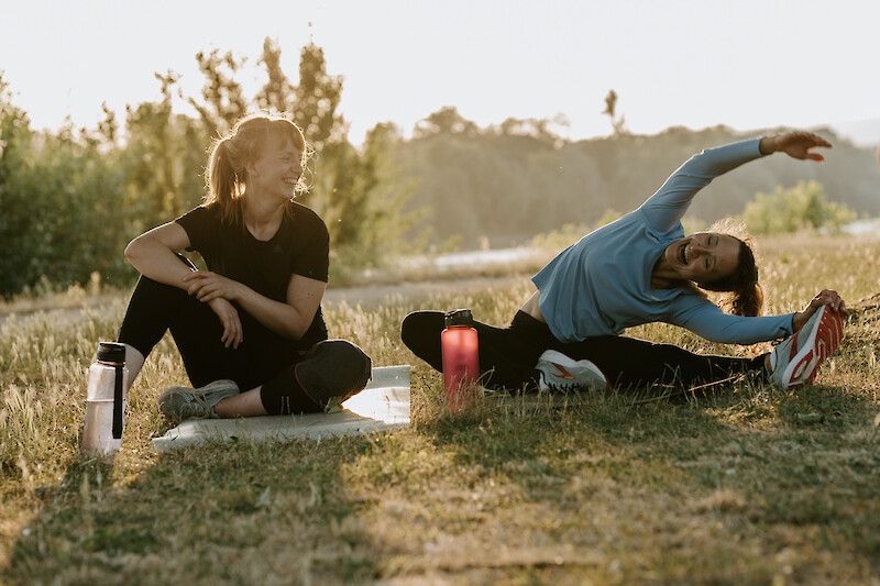 Zwei Frauen beim Dehnen im Freien während ihres Zirkeltrainings zuhause – Bewegung, Spaß und Motivation bei Original Bootcamp.