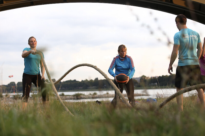 Outdoor-Fitness Training mit Battle Ropes und Medizinball am Wasser in einer kleinen Gruppe.