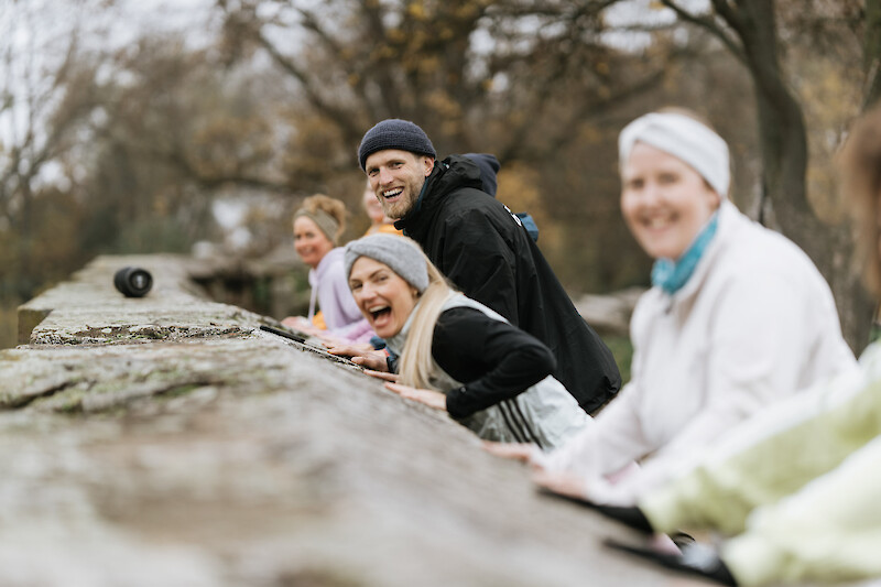 Outdoor Gym Push-ups an der Mauer – Gruppe macht erhöhte Liegestütze an einer Steinmauer, mit viel Dynamik und lachenden Gesichtern.