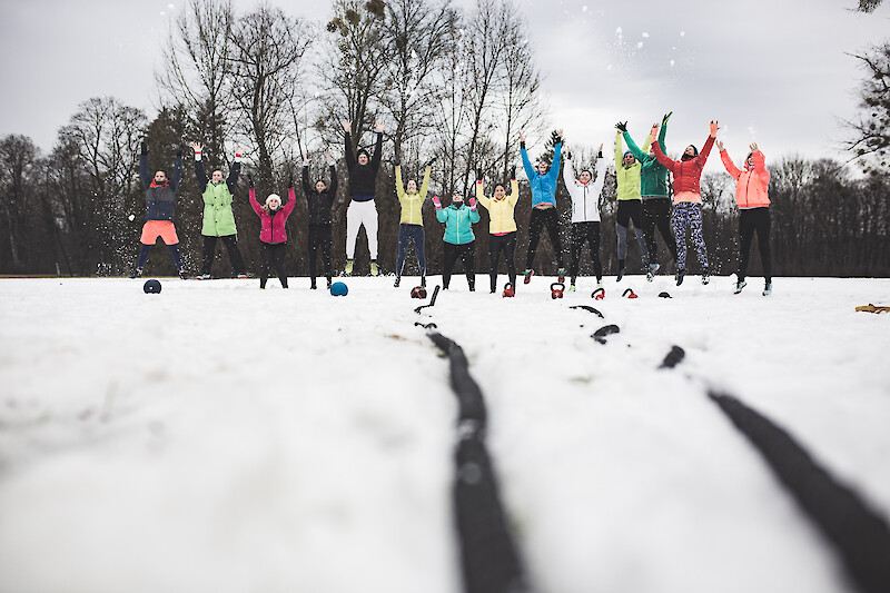 Outdoor winter training mit Gruppenworkout im Schnee: Menschen springen gemeinsam beim Outdoor-Fitness-Training im Winter im Park