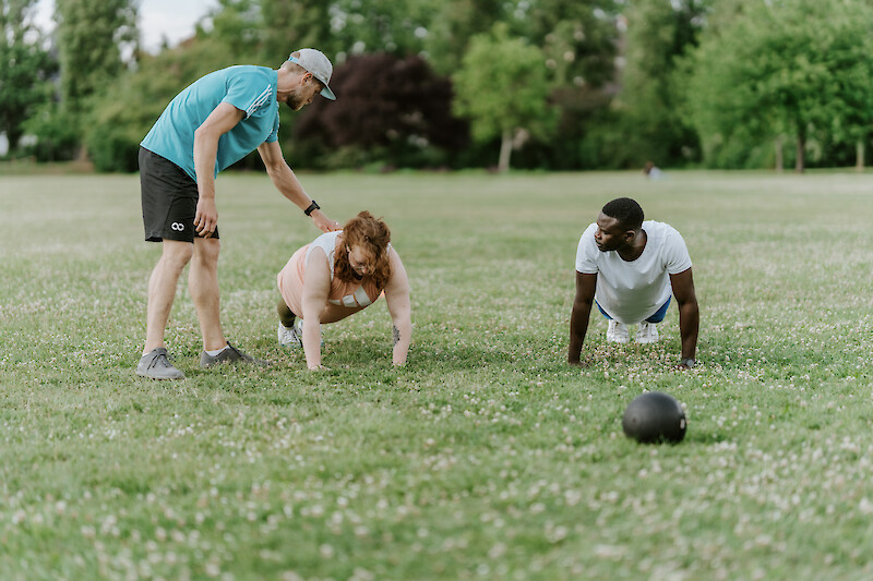 OutdoorFitness Düsseldorf beim Core-Training im Park, Teilnehmende absolvieren Stützpositionen mit individueller Anleitung durch einen Trainer.