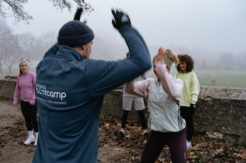 Outdoor Fitness Kiel: Trainer motiviert Teilnehmerin beim Outdoor-Workout im Park, Gruppentraining mit Functional Fitness bei herbstlichem Wetter.