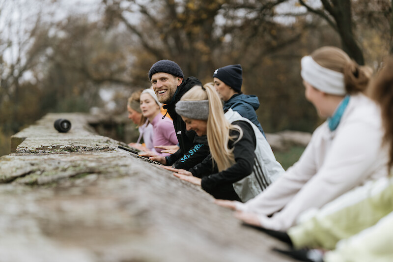 Outdoor Fitness Kiel: Gruppentraining im Park mit funktionellen Übungen an einer Steinmauer, gemeinsames Outdoor-Workout bei herbstlicher Stimmung.
