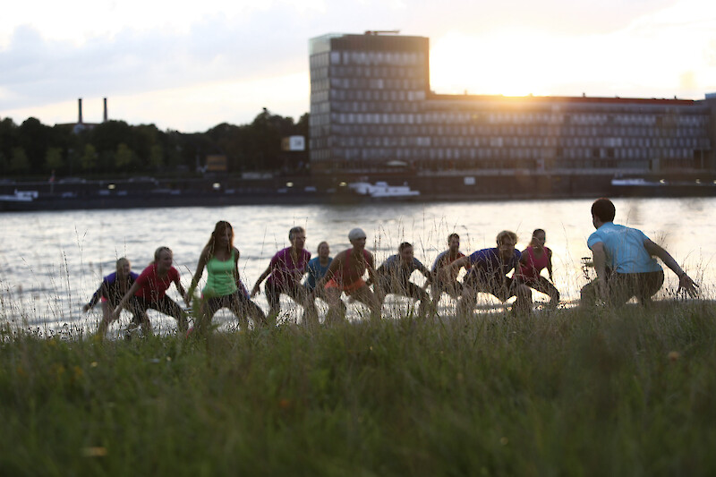 Zirkeltraining in Köln als Gruppenworkout am Rhein bei Sonnenuntergang mit funktionellen Kniebeugen